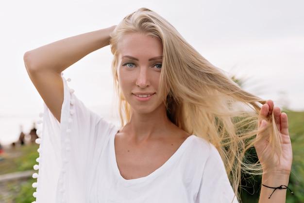 Woman with blonde hair smiling in white blouse outdoors