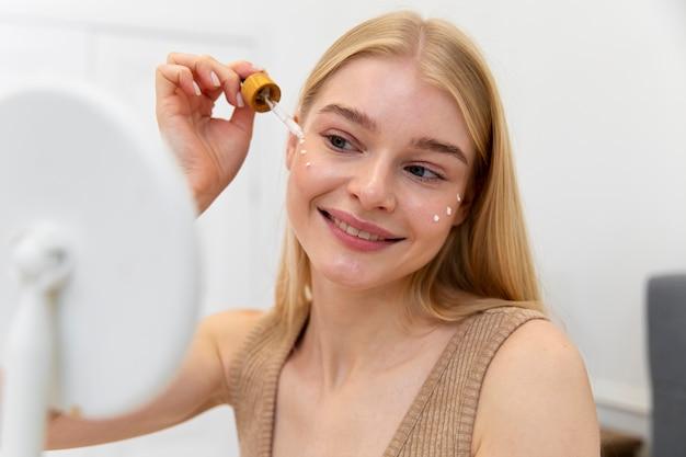 Smiling woman applying serum with dropper to face