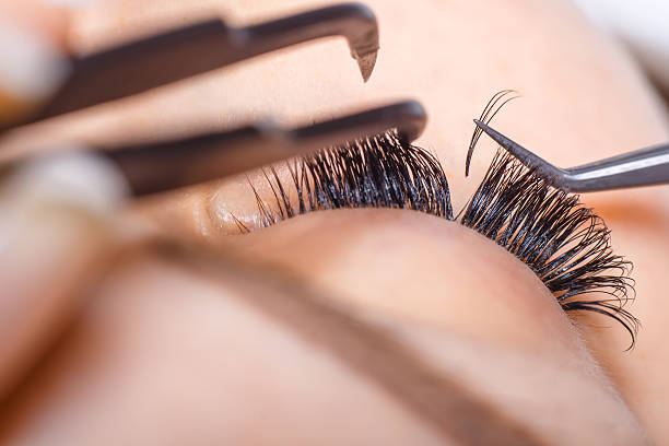 Close-up of eyelash extension procedure. Professional beautician applying artificial lashes to a client's natural eyelashes.