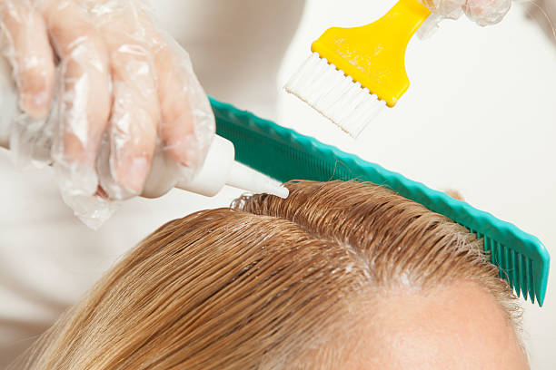 Hairdresser applying hair dye to client's hair with brush and comb in a salon